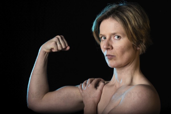 Low key studio portrait of a 35 year old white woman with naked shoulders showing her biceps, Brussels