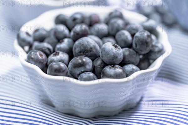 Blueberries in a small white bowl on a light blue background, close up