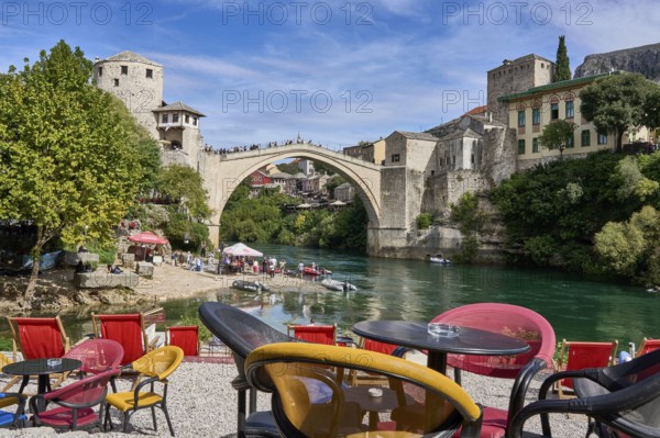 Cafe with colourful chairs on the bank of the river Neretva, behind the bridge Stari Most, numerous tourists, old town of Mostar, Bosnia-Herzegovina