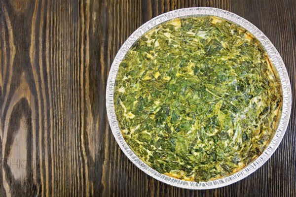 Celtic cake with spinach, tomatoes, oatmeal and eggs in baking dish from a foil against the backdrop of wooden planks on top