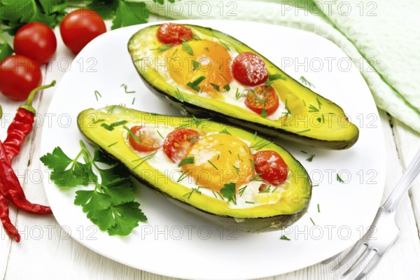 Scrambled eggs with cherry tomatoes in two halves of avocado in a plate, kitchen towel and fork on the background of wooden boards