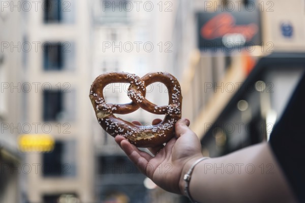 Woman hand holding a pretzel against cityscape. Focus on bread, blurred background