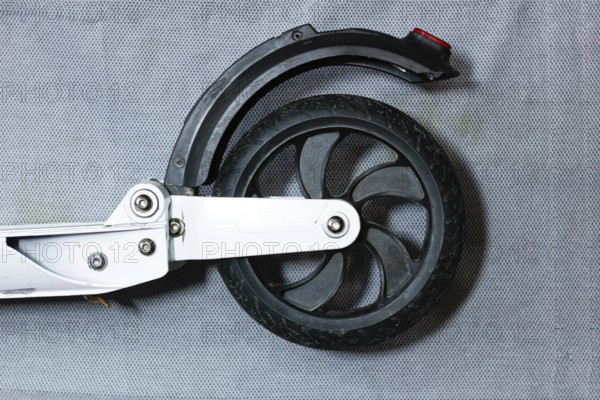 Close-up of a scooter's rear wheel with a sleek black tire and metal frame on a grey background