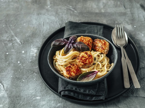 Zucchini Parmesan Meatballs with Pasta Carbonara in black craft plate over gray background. Close up view of creamy carbonara with copy space left