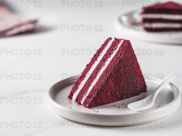 Piece of red velvet cake with perfect texture in matte plate on white marble tabletop. Slice of delicious homemade red velvet cake with raspberry and chocolate. Copy space for text