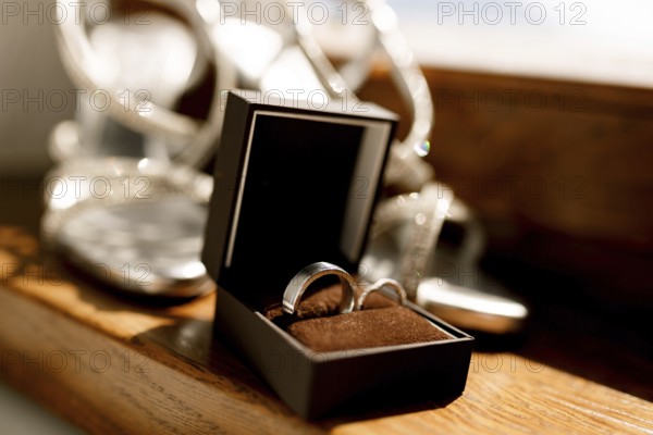 Wedding rings in an open brown box on the floor with women's wedding sandals on a blurred background.
