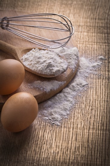 Flour in spoon eggs and corolla on vintage wooden board food and drink concept