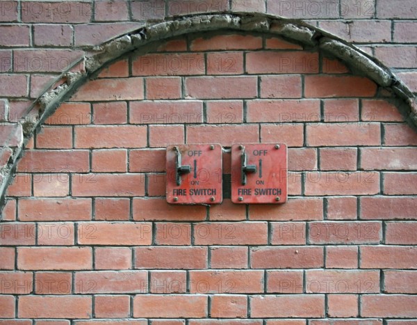 Two old red metal fire switches on an exterior brick wall