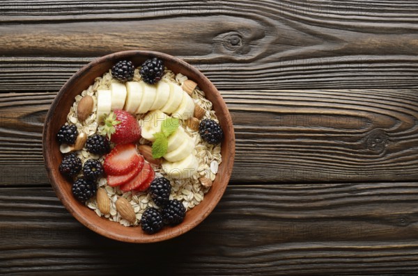 Flat lay top view at Fruit healthy muesli with banana strawberry almonds and blackberry in clay dish on wooden kitchen table