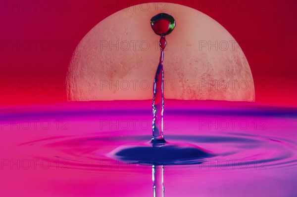A drop of water rises into the air in front of a large full moon and in a pink-red sky, Planet Pluto Highspeed Photography, Composing, Grenzach- Wyhlen, Baden- Württemberg, Germany