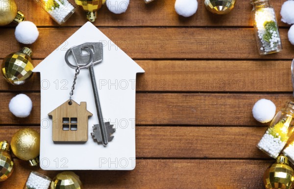 Key to house with a keychain tiny home on wooden background with Christmas decor layout. Gift for New Year, Christmas. Building, project, moving to new house, mortgage, rent and purchase real estate
