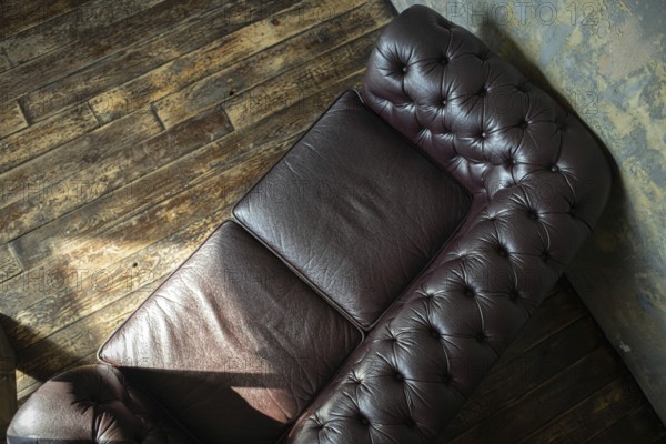 Top view of a vintage tufted leather couch against a wooden floor and textured wall