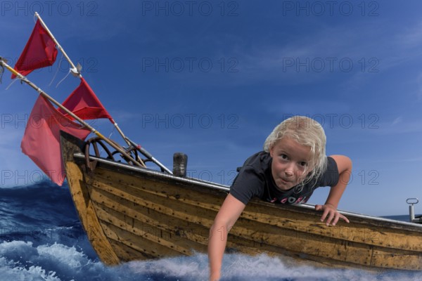 Child in a wooden boat with waves and holding his hand in the water