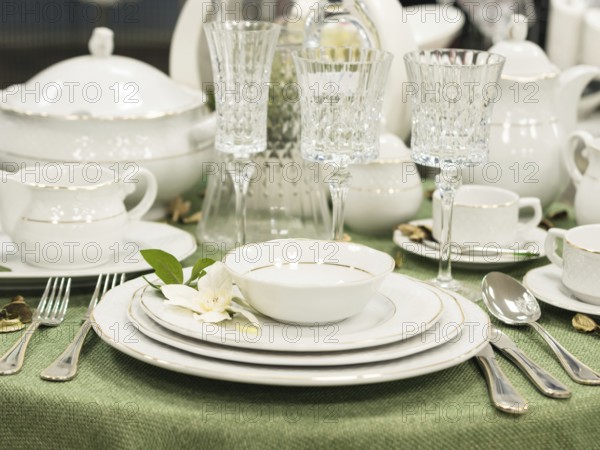 Set of new dishes on table with green tablecloth. Stack of white plates with flowers on restaurant table. Shallow DOF