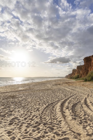 Incredible rock formations by the sea. Red cliffs with red earth and breathtaking formations on the wide sandy beach, which is bathed in warm light by the sun at sunset. Praia da Falésia, Algarve, Portugal