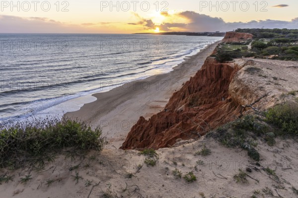 View from one, eroded cliffs of red sand and pebbles with stunning formations illuminated by a warm sunset. Wide beach on the Atlantic Ocean in a landscape shot. Praia da Falésia, Algarve, Portugal
