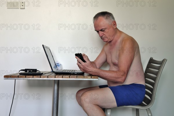 Businessman, freelancer, 60 plus on holiday working with laptop and mobile phone, Pattaya, Chonburi, Thailand