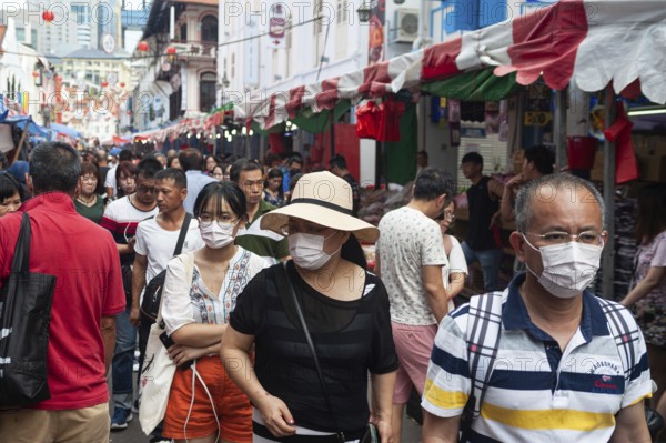 24.01.2020, Singapore, Republic of Singapore, Asia, Pedestrians wearing face masks stroll through a busy street bazaar in the Chinatown district, which takes place every year for Chinese New Year. This comes shortly after the first coronavirus infection was confirmed in the city-state