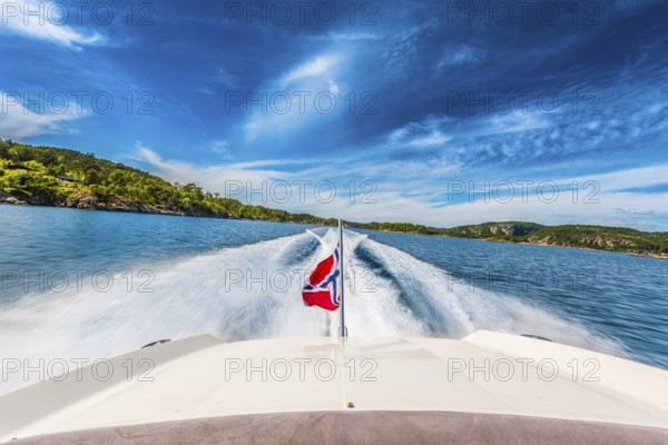 Speed boat swiftly crossing a sunny fjord in southern Norway sporting the Norwegian flag. 2017-06-27