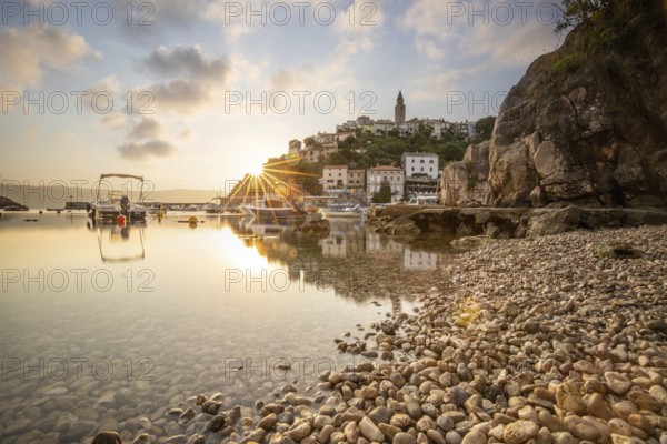 Harbour and beach with an old village on a hill. Boats are reflected in the water, the sun rises on the Adriatic horizon. Beautiful landscape shot from Vrbnik, Krk, Croatia
