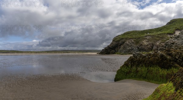 View of the picturesque golden sand Maghera Beach with algae-covered rocks and cliffs in the foreground