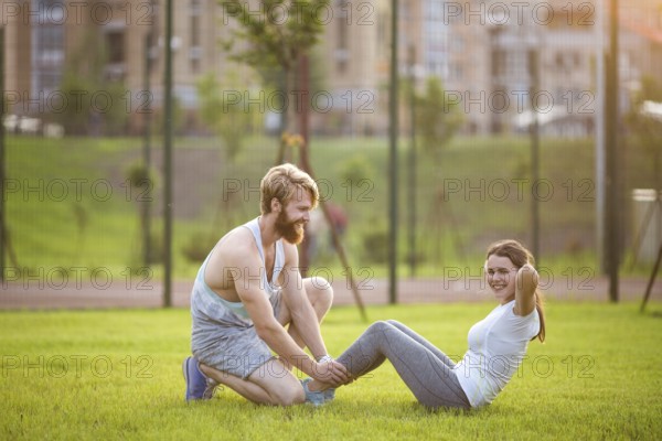 Sit ups fitness couple exercising sit up outside in graß Fit people working out cross training. Woman doing abdominal crunches press exercise with trainer. Couple Doing Sit-Ups Abdominal Crunch