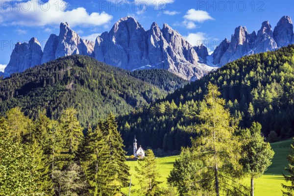 Dolomites, Tirol. Sunny warm autumn day. Rocky peaks and forested mountains surrounded by green Alpine meadows. The symbol of the valley Val di Funes - church of Santa Maddalena