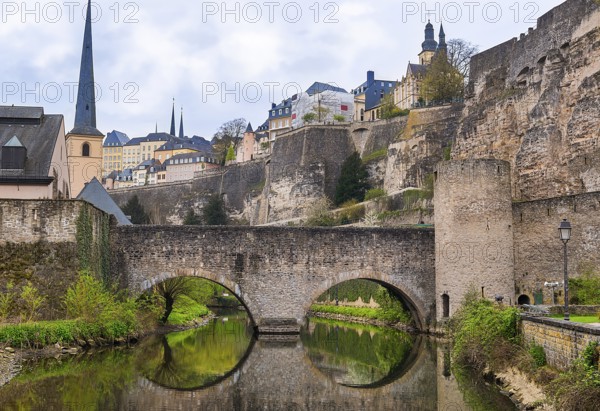 Stone bridge reflected in the water, and the ruins of a former famous castle, representing the culture and history of Luxembourg in the Middle Ages