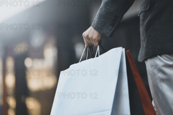 Close up of a young caucasian man holding some different paper shopping bags in the street