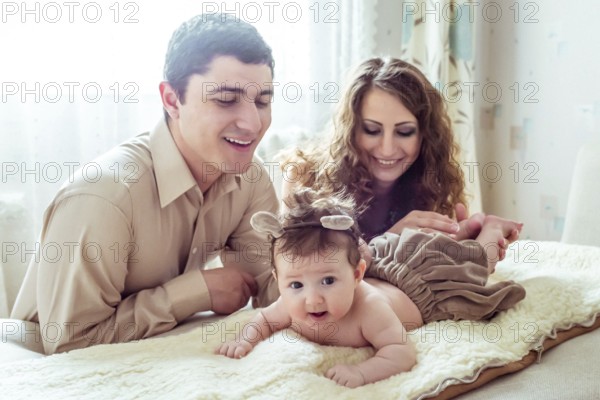 Naked baby with her parents lying on soft blanket in the room