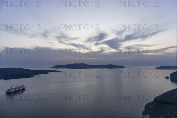 Evening atmosphere after sunset over the island of Thirassia, cruise ship in the archipelago of Santorini, Cyclades, Greece