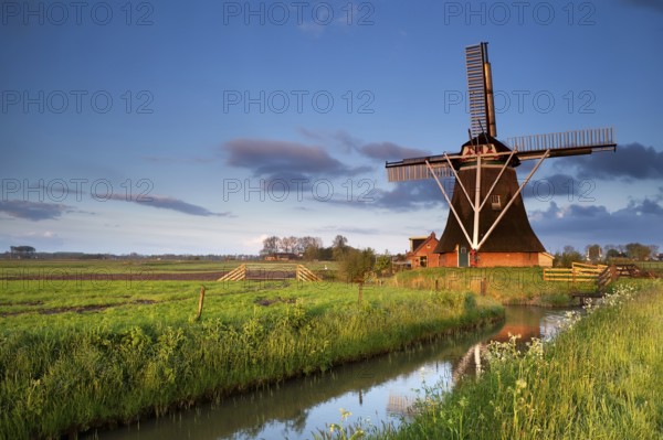 Dutch windmill reflected in river in morning sunrise sunlight, Holland