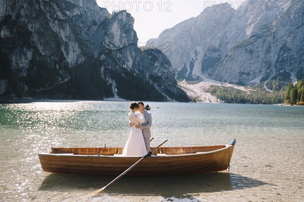 Bride and groom sailing in wooden boat, with oars at Lago di Braies lake in Italy. Wedding in Europe - Newlyweds are standing embracing in a boat
