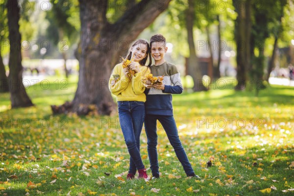 Friendship between siblings. Siblings together outside with bright coloured background. Kids autumn portrait. Brother and sister playing in autumn park leaves. Family active fall weekend concept