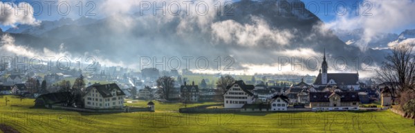 Panorama over the village of Schwyz, Switzerland with wisps of fog and clouds in oblique sunlight, Schwyz, Switzerland