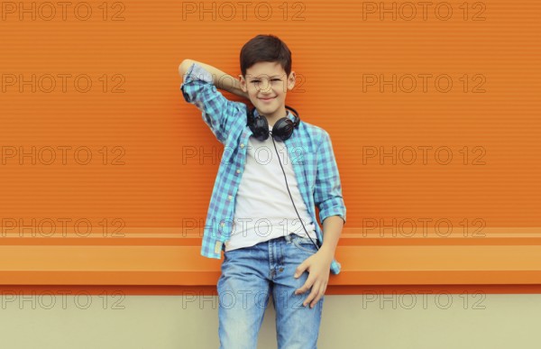 Portrait of happy modern teenage boy listening to music with headphones in the city on orange wall background