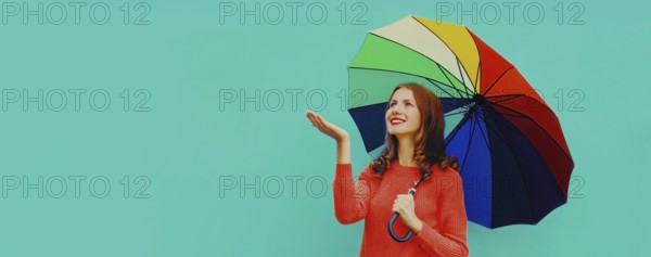 Autumn portrait of happy smiling young woman holding colorful umbrella wearing red knitted sweater on blue background