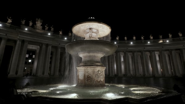 An illuminated night view of a flowing fountain surrounded by columns, Fontana del Bernini, St. Peter's square, Rome, Lazio, Italy