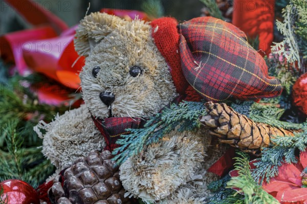 Close up of a Christmas decoration with red Christmas baubles, red candles, a green fir tree and a teddy bear
