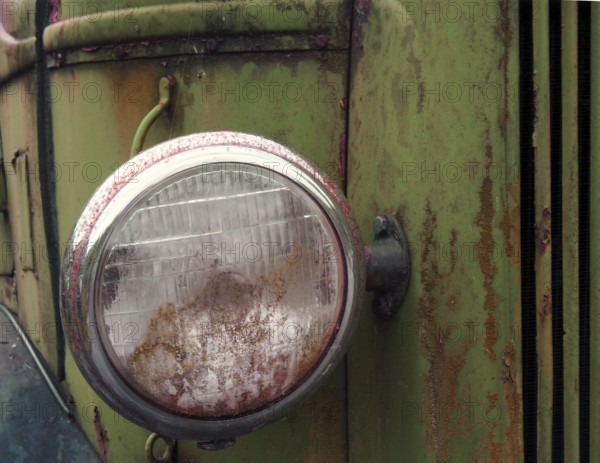 Close up of the headlight of an old abandoned truck with rusted green grille and panels