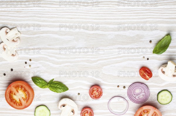 Food cooking background: arranged fresh ingredients, basil, cherry tomatoes, mushrooms, cut cucumber, onion, chilli pepper, spices on white wooden background top view, space for text, food photography