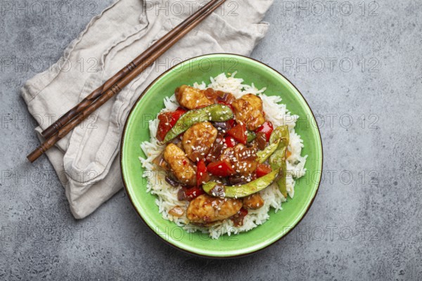 Asian sweet and sour sticky chicken with vegetables stir-fry and rice in ceramic bowl with chopsticks top view on gray rustic stone background, traditional Asian dish, food photography, food photography