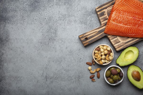 Food sources of healthy unsaturated fat and omega 3: fresh raw salmon fillet, avocado, olives, nuts on cutting board, rustic stone background top view. Healthy nutrition and keto diet, space for text, food photography, food photography