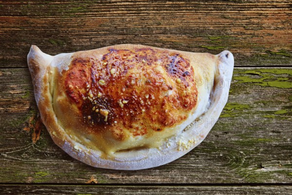 Pizza Calzone folded as a patty on a wooden board table