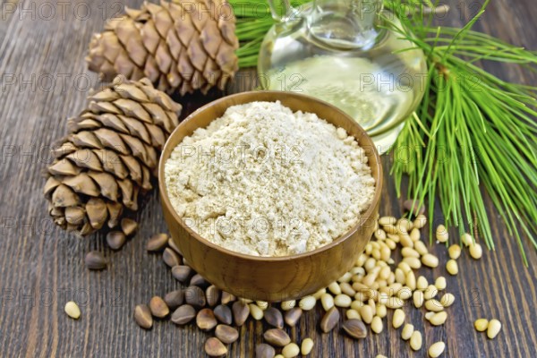 Flour cedar in a wooden bowl, cedar nuts and two cones, the oil in the glass carafe, cedar branch against the backdrop of wooden planks
