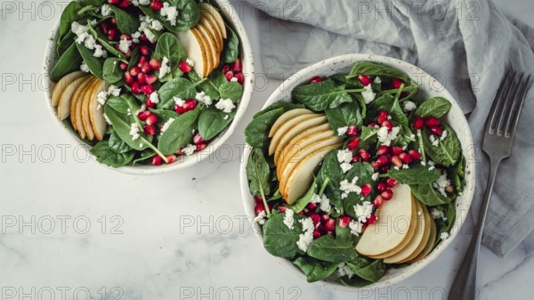 Fresh salad with baby spinach, pear, pomegranate and cottage cheese. Two bowls with delicious summer fruit salad on marble table. Copy space for text. Ideas and recipes for healthy breakfast or lunch
