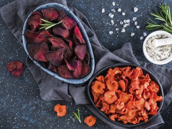 Baked beet and carrot slices with coarse sea salt scented rosemary. Vegan diet food idea and recipe. Healthy homemade beetroot and carrot chips in plate and ingredients on dark blue background. Copy space. Top view