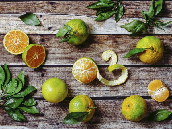 Green mandarines on old wooden background. Fresh ripe half, whole and peeled green tangerines with leaves, top view or flat lay