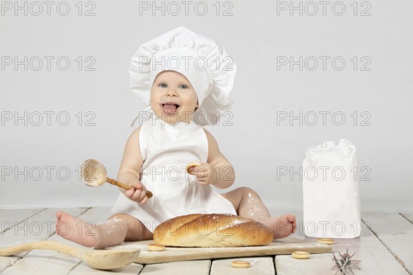 Child cooking. Beautiful little girl in cooking clothes with a long loaf of bread and flour. The child is one year old. Funny baby laughs. Little cook. The concept of baking bakery products