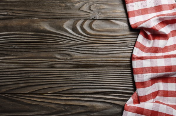 Red checkered napkin on brown wooden kitchen table with copy-space. Top view